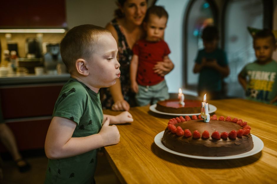 A child blowing out a candle on a chocolate birthday cake topped with raspberries