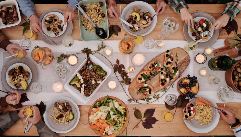 Overhead view of friends sharing vegetable dishes, salads and pasta at a candlelit table