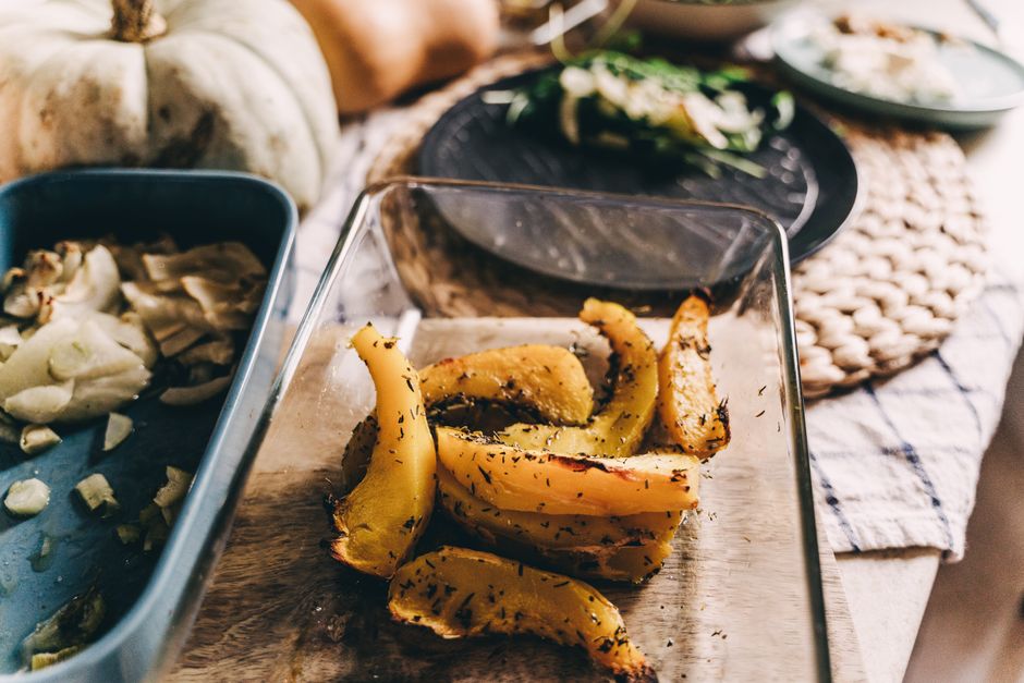 Roasted squash wedges in a glass baking dish on an autumn table with pumpkins